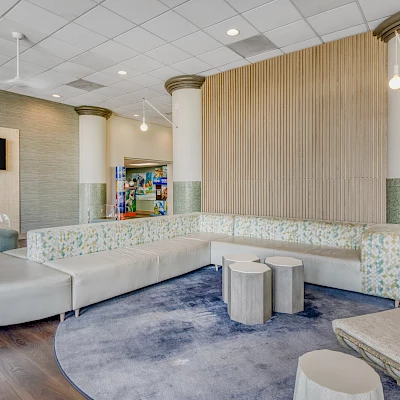A modern lounge area with a curved sofa, round tables, chairs, and a circular rug, set against a backdrop of decorative columns.