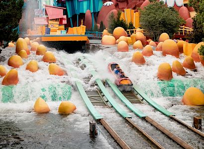 This image depicts a colorful, animated-themed water ride at an amusement park, with boats on tracks surrounded by whimsical decor and water splashes.