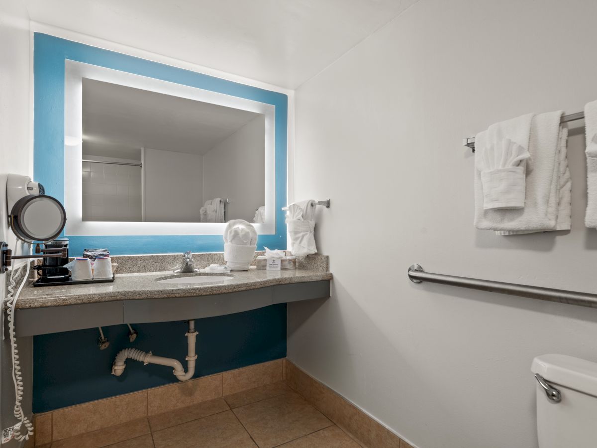 A clean, modern bathroom with a large mirror, blue accent wall, sink, towels, a hairdryer, and toiletries sitting on the countertop, ending the sentence.