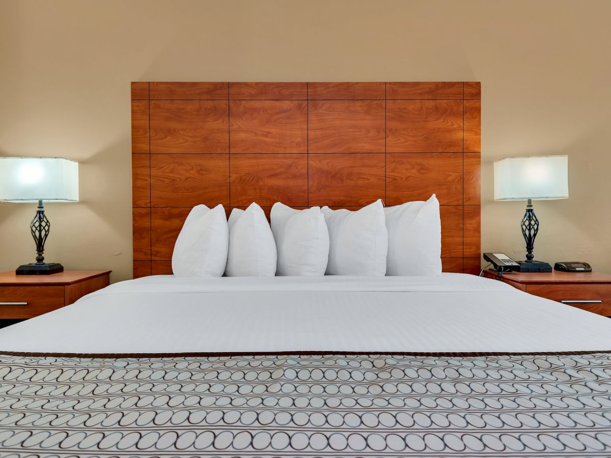 A neatly made bed with white pillows, flanked by two nightstands, each with a stylish lamp. The room has a warm, cozy ambience and wooden headboard.