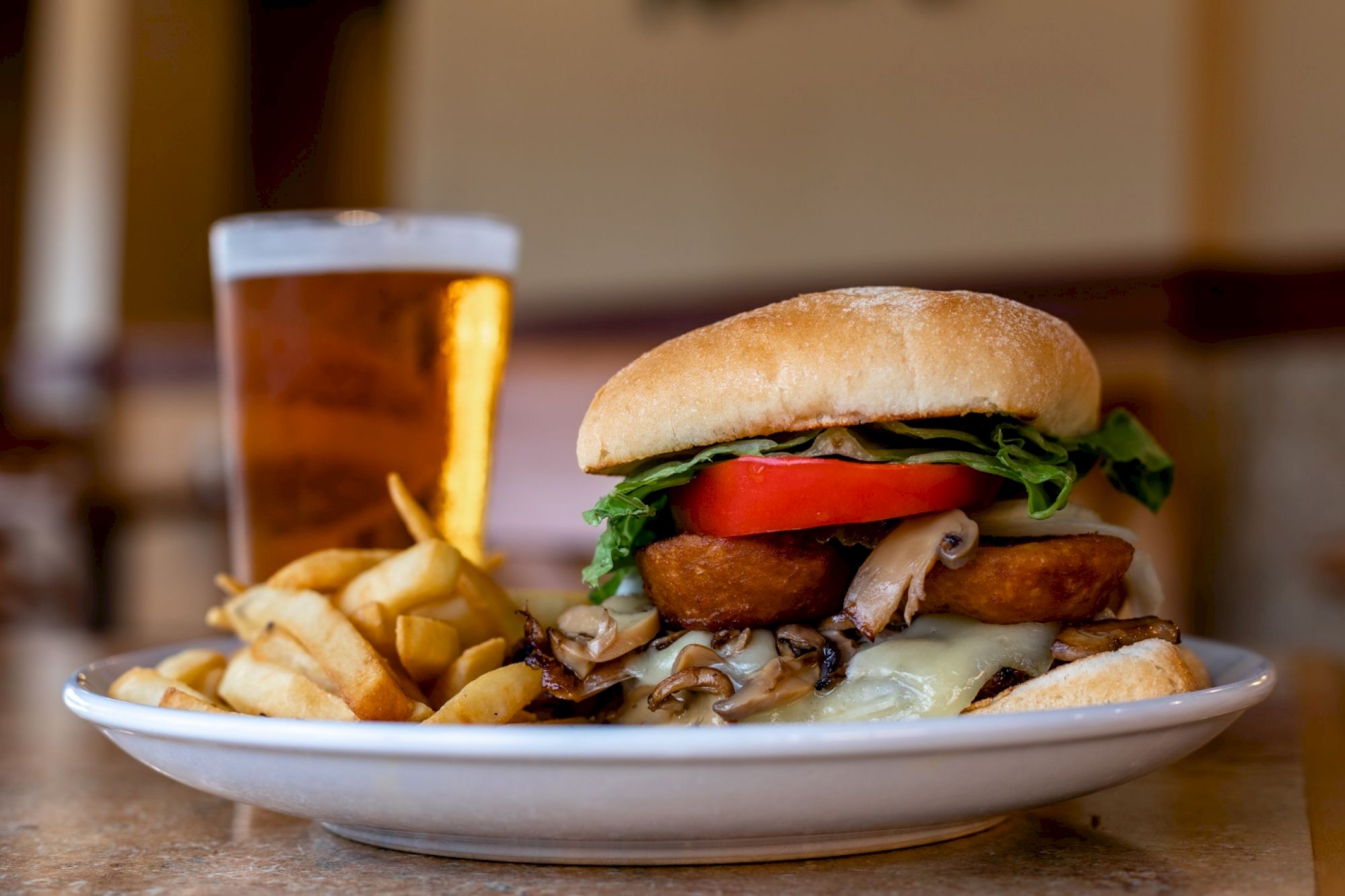 A delicious burger with fries and a cold beer are served on a plate against a blurred background.